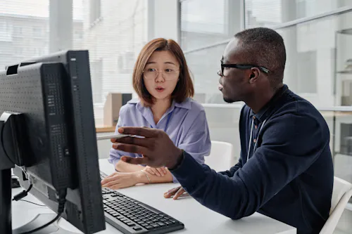 Cybersecurity analyst pointing at computer monitor and discussing computer program with his colleague