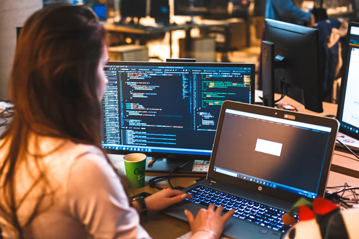 Woman coding on two computer screens