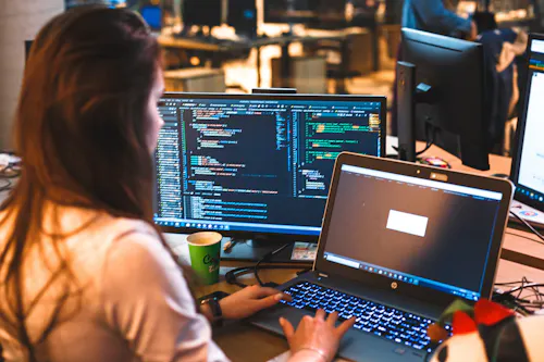 Woman coding on two computer screens