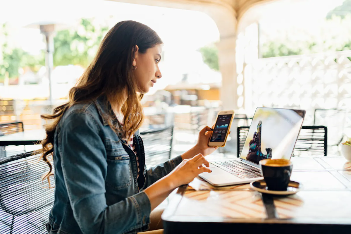 A student works on a laptop and smartphone at a coffee shop.