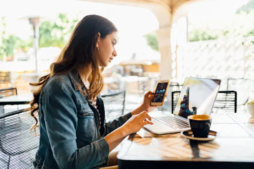 A student works on a laptop and smartphone at a coffee shop.