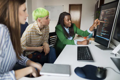 A coding instructor points out a line of code to students on a monitor.