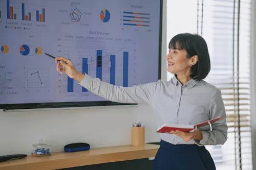 A data analyst presents results in a meeting using a whiteboard.