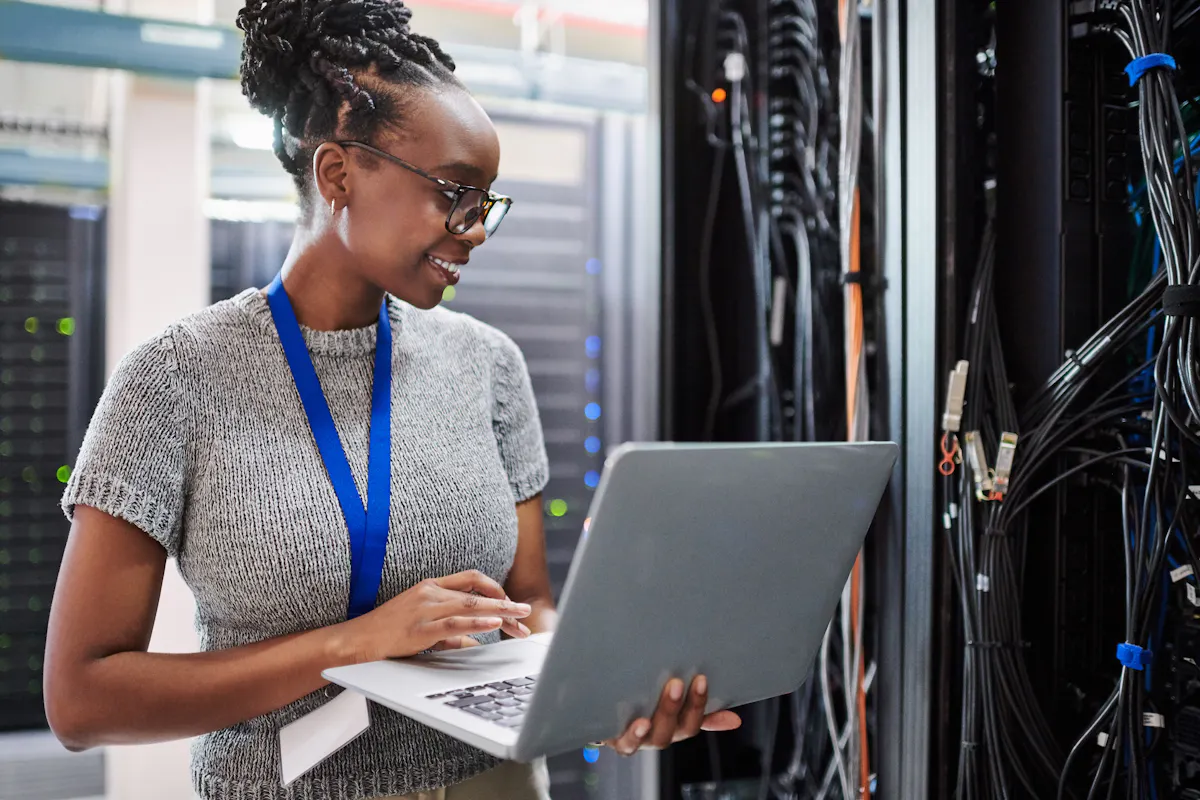 Young database administrator works on a laptop in a server room