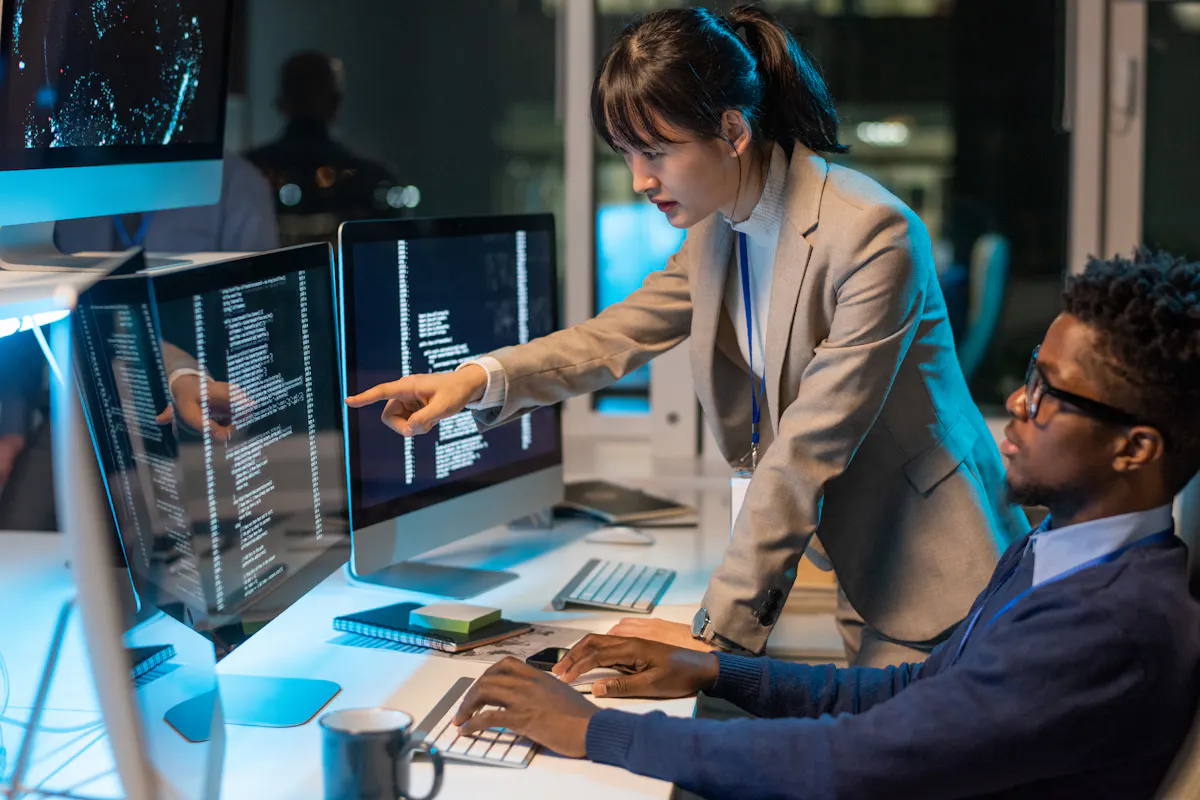 Two IT engineers reviewing code on a monitor.