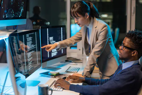 Two IT engineers reviewing code on a monitor.