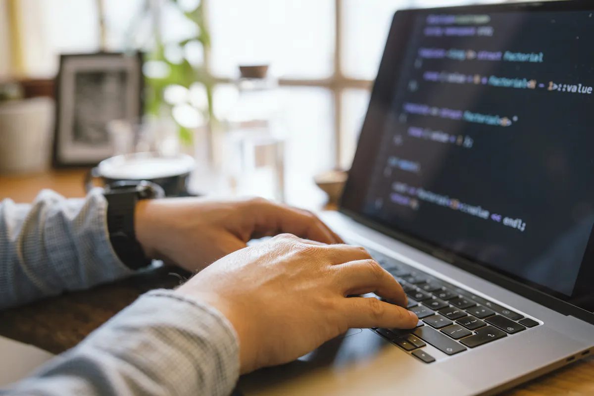 A computer programmer types code on a laptop.