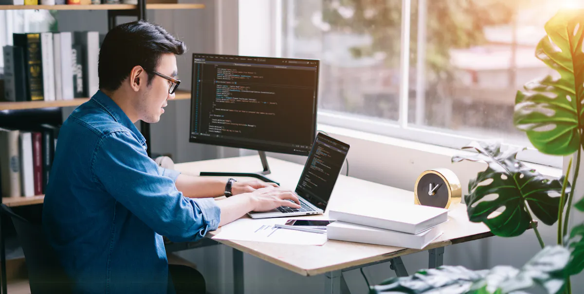 A programmer types code on a laptop.