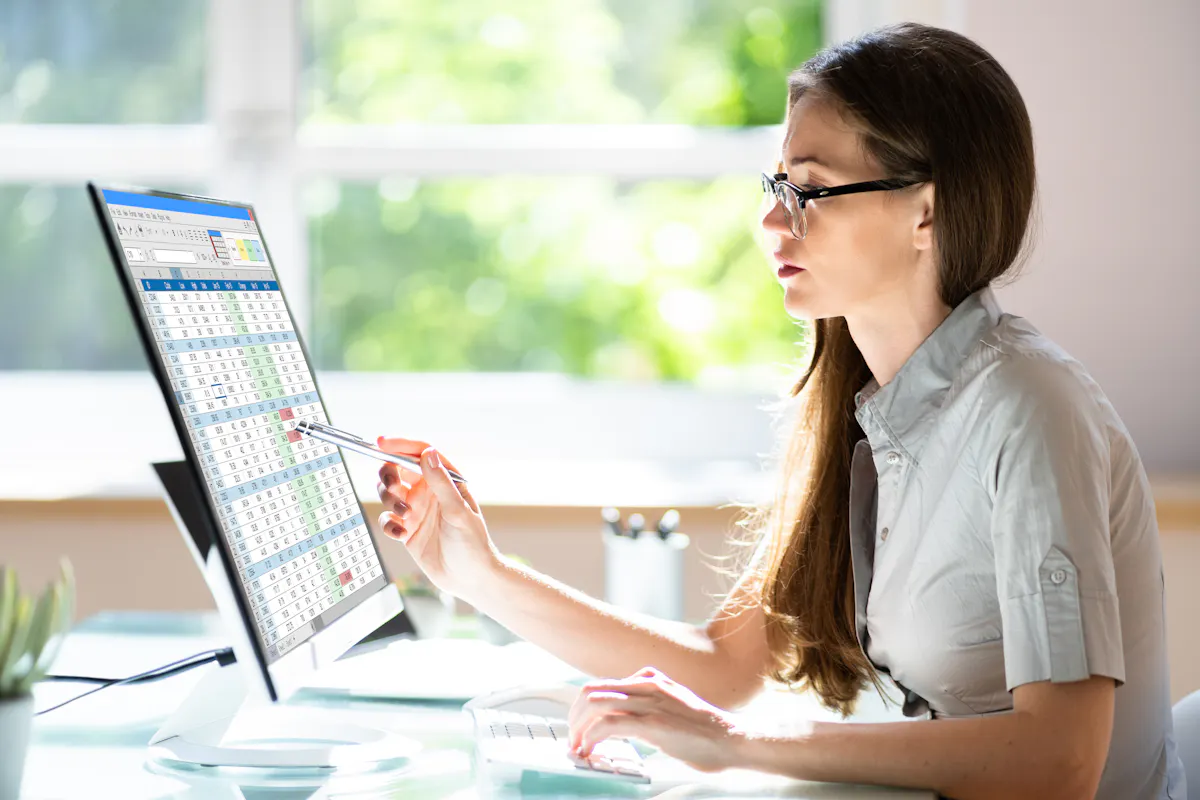 A data analyst uses a spreadsheet on a desktop monitor.