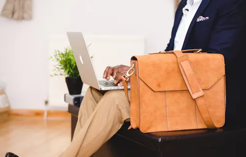 Person with laptop open on lap and briefcase next to them