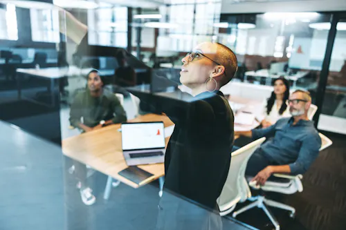 A product manager explains data on a display screen to other team leaders.